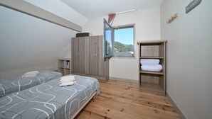 Un dormitorio con dos camas, un armario, una estantería con toallas y una ventana con vistas a colinas.