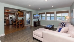 A spacious living area with a large window offering a view of the water, a cozy seating area, and a kitchen with modern appliances.