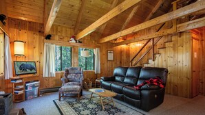 Ein Holzblockhaus-Interieur mit einem Ledersofa, einem Sessel und einem Fernseher auf einem Holzständer.
