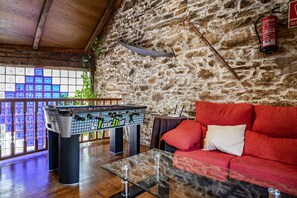 A room with a foosball table, a red sofa, a glass coffee table, and a stone wall.