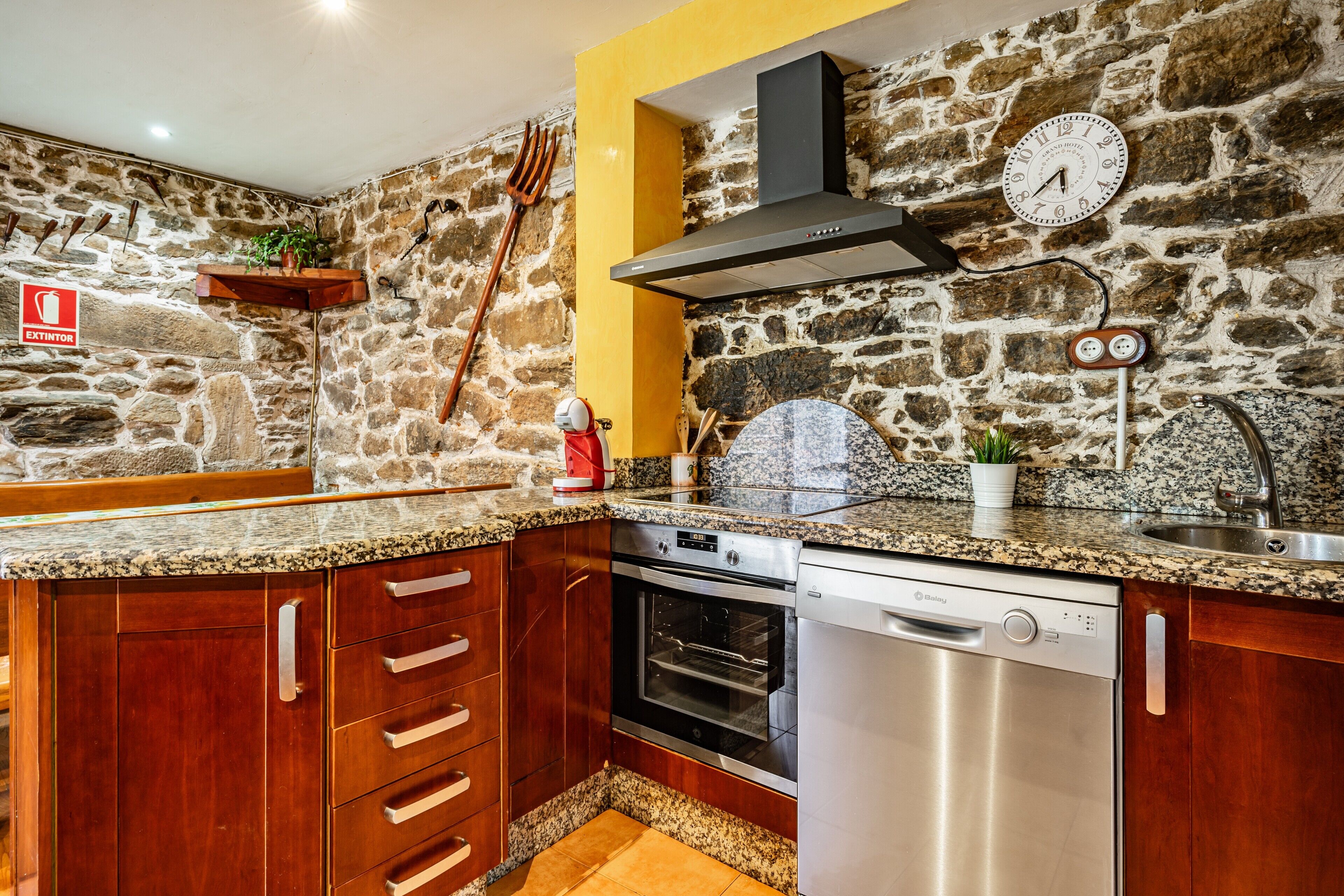 Una cucina con pareti in pietra, mobili in legno, forno in acciaio inossidabile e lavastoviglie.