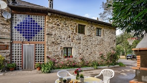 Un bâtiment en pierre avec une fenêtre à carreaux, des sièges à l’extérieur et des plantes en pot.