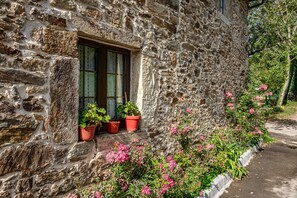 Un bâtiment en pierre avec une fenêtre, des plantes en pot et des fleurs roses.