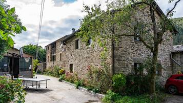 A stone building with a basketball hoop, a red car, and a tennis table in the foreground.