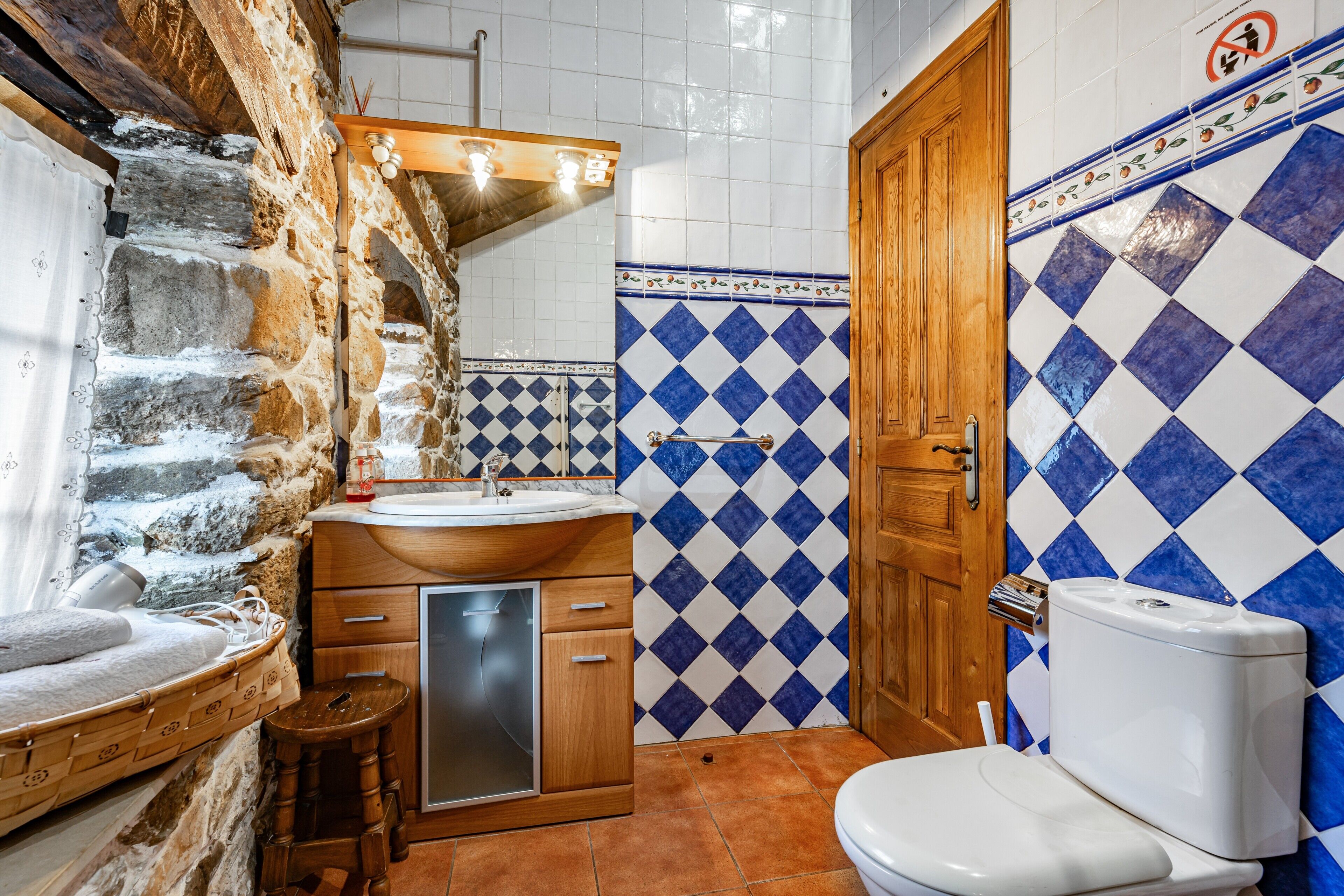 Un baño con pared de piedra, puerta de madera, lavabo e inodoro.