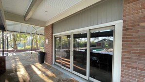 A covered patio area with stone flooring, a brick wall, and a glass door leading to an outdoor space with a pool and tables. - One-of-a-Kind Railcar Retreat with Pool (Tylertown)