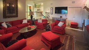 A spacious living room with red sofas, a coffee table, and a patterned rug. A television is mounted on the wall, and a deer head decoration is visible. - One-of-a-Kind Railcar Retreat with Pool (Tylertown)