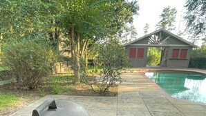 A barbecue grill on a tiled patio with a pool in the background. - One-of-a-Kind Railcar Retreat with Pool (Tylertown)