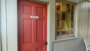 A red door with a "Restroom" sign, a window with stained glass, and a white chair outside. - One-of-a-Kind Railcar Retreat with Pool (Tylertown)
