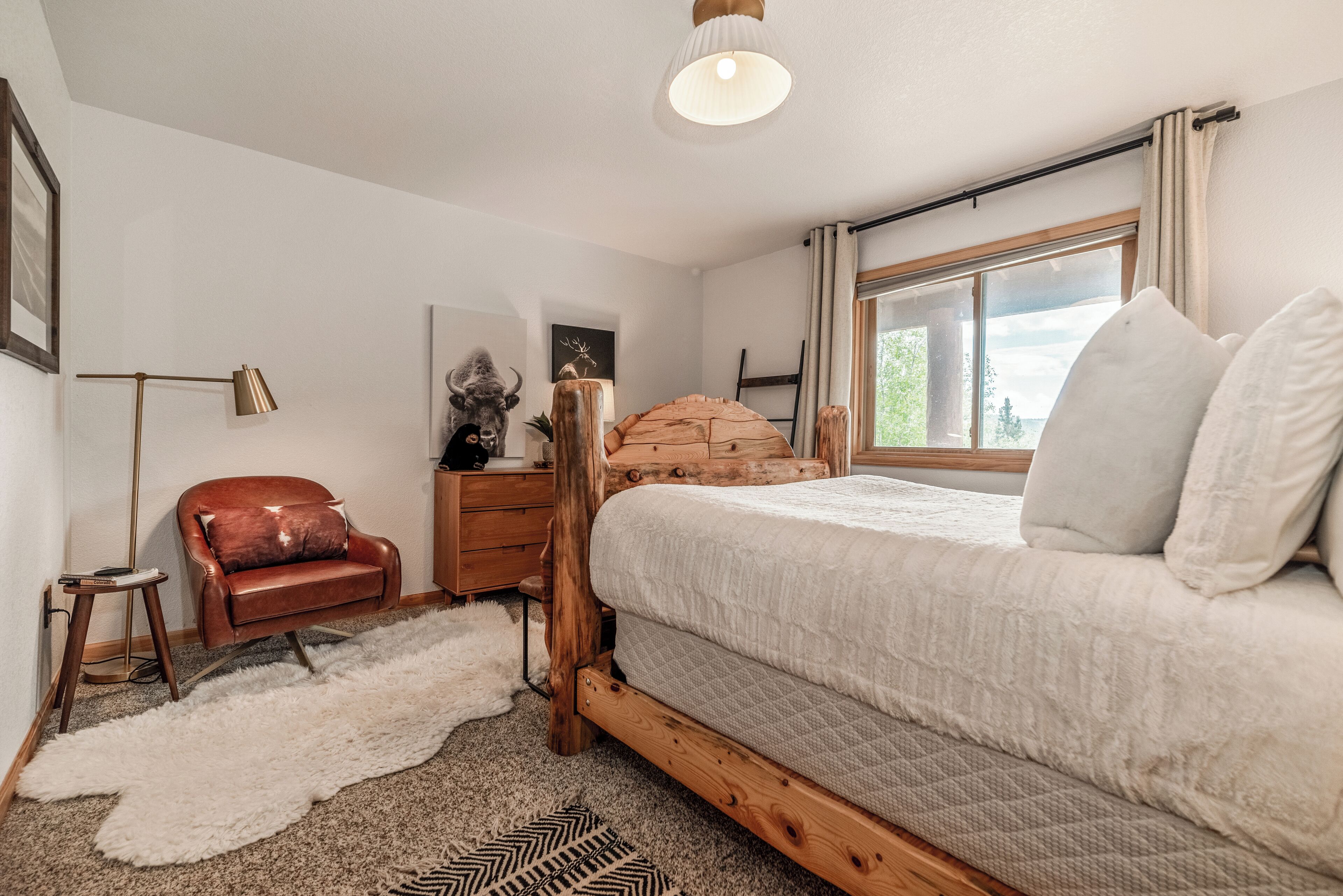 A bedroom with a wooden bed frame, a red leather chair, a white rug, and a large window with curtains.