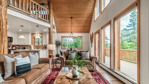 A spacious living room with a high ceiling, a wooden balcony, and large windows offering a view of the outdoors.