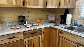 A kitchen with wooden cabinets, a granite countertop, a coffee maker, a pumpkin, and kitchen towels.
