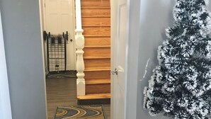 En hall med en trätrappa, en mönstrad matta, ett litet julgran och en dörr som leder till ett annat rum.
