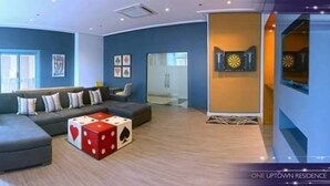 A modern living room with a sectional sofa, a coffee table with dice, and a wall clock. - One Uptown Residence (Taguig)