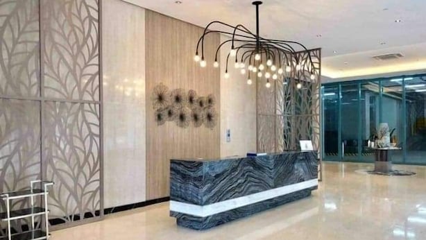 A modern reception area with a marble counter, decorative wall panels, and a unique lighting fixture. - One Uptown Residence (Taguig)