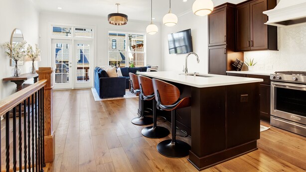 A modern kitchen with a central island, bar stools, and a dining area with a sofa. - Luxe New Construction with River View, Pool Table (Savannah)