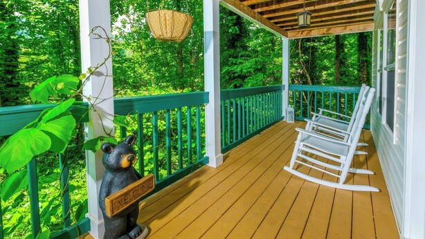 Eine Holzterrasse mit einem Schaukelstuhl und einer Bärenstatue auf einer Veranda mit grünem Geländer.