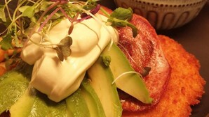 Un piatto chiamato Cotoletta di Elefante con fette di avocado, germogli e un cucchiaio di salsa.