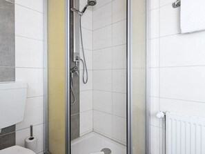 Une salle de bain moderne avec une douche à parois de verre, des carreaux blancs et un porte-rouleau de papier toilette visible.