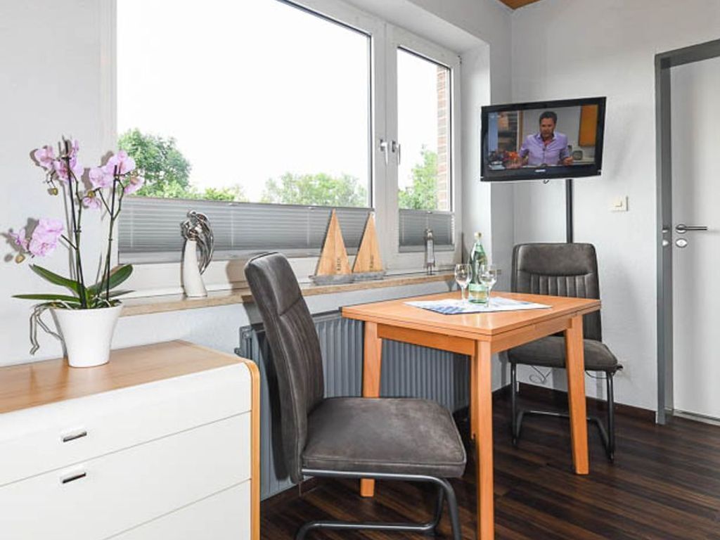 Ein modernes Zimmer mit einem Holztisch, zwei Stühlen, einem Fernseher, einer Topfpflanze und einem Fenster mit Jalousien.