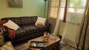 A living room with a plaid sofa, a coffee table with books and a vase, a painting of flowers on the wall, and patterned curtains. - Relaxing, Peaceful 1-bedroom Pet- Friendly Apartment  (Mason City)