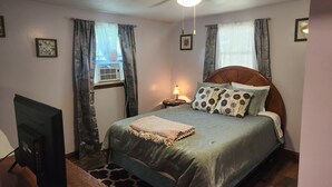 A bedroom with a bed, a ceiling fan, a bedside lamp, and a window with curtains. - Relaxing, Peaceful 1-bedroom Pet- Friendly Apartment  (Mason City)