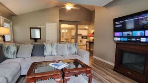 Una sala de estar con un sofá modular, una mesa de centro de vidrio y un televisor de pantalla plana montado en la pared.