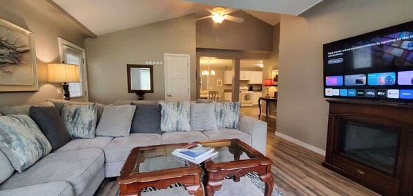 A living room with a sectional sofa, a glass coffee table, and a flat-screen TV mounted on the wall.