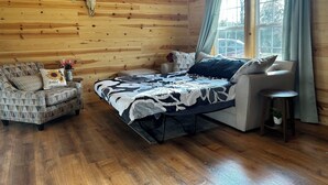 A cozy cabin room with wooden walls, a bed with a patterned bedspread, a sofa, and a small table with a plant. - Texas Longhorn Ranch-Private Cabin-Pasture Views (Licking)