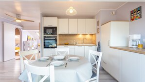 A modern kitchen with white cabinetry, a dining table set for four, and a hanging pendant light. - Apartment 'Les Hauts Du Lac' with Lake View and Wi-Fi (Les Sables-d'Olonne)