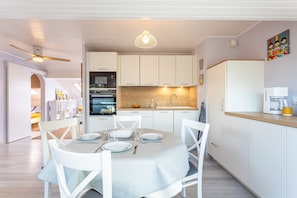A modern kitchen with white cabinetry, a dining table set for four, and a hanging pendant light.