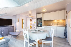 A modern kitchen with white cabinets, a dining table set for four, and a television in the living area.