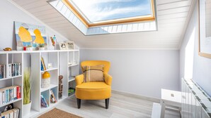 A room with a skylight, a yellow armchair, a bookshelf, and a white radiator. - Apartment 'Les Hauts Du Lac' with Lake View and Wi-Fi (Les Sables-d'Olonne)