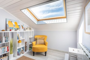 A room with a skylight, a yellow armchair, a bookshelf, and a white radiator.