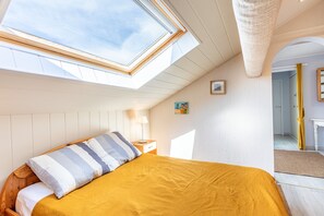 A bedroom with a skylight, a bed with a striped pillow, a bedside table, a lamp, and a small painting on the wall.