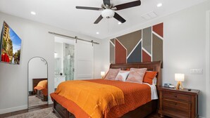 A modern bedroom with a large bed, a nightstand, a ceiling fan, and a mirror.