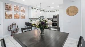 A modern kitchen with white cabinets, a dark wooden dining table, and a vase of flowers.