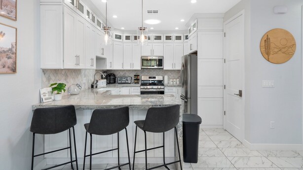 A modern kitchen with white cabinets, a marble countertop, and black bar stools.