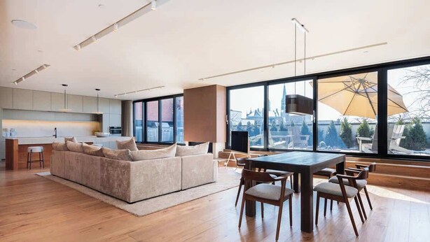 A spacious living area with a large window, a sofa, a dining table, and a kitchen in the background. - Luxury 3+ BR Penthouse Near Jean-Talon Market (Montréal)