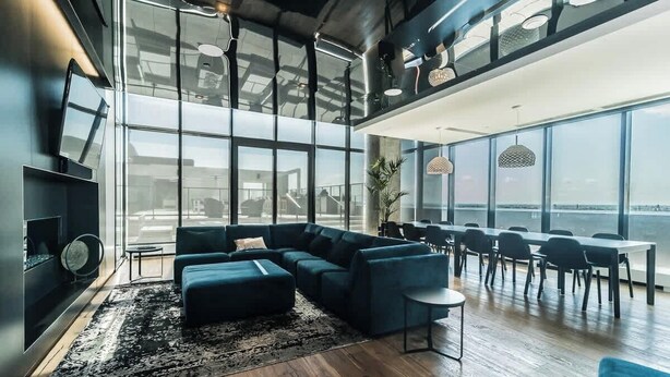A modern interior with a sectional sofa, a dining area, and large windows offering a view.