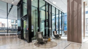 A modern lobby with glass doors, two armchairs, and a tiled floor.
