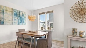 A dining area with a wooden table, grey upholstered chairs, a hanging light fixture, and a large abstract painting on the wall. - Family-Friendly Home with Rooftop Lounge (Inlet Beach)