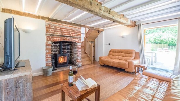 A cozy living room with a brick fireplace, a leather sofa, a wooden coffee table, and a television.