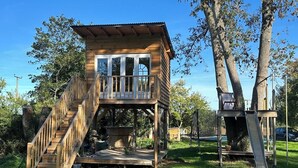 A wooden treehouse with a balcony and a slide, surrounded by trees and grass.
