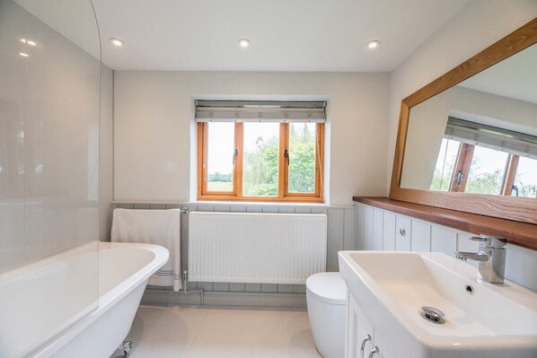 Une salle de bain moderne avec une baignoire, un lavabo et une fenêtre donnant sur un paysage verdoyant.