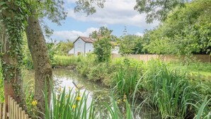 A serene riverside setting with a white building, lush greenery, and a wooden fence.