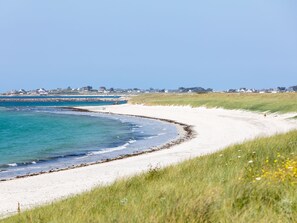 Een kuststrand met wit zand, helderblauw water en een grasduin.