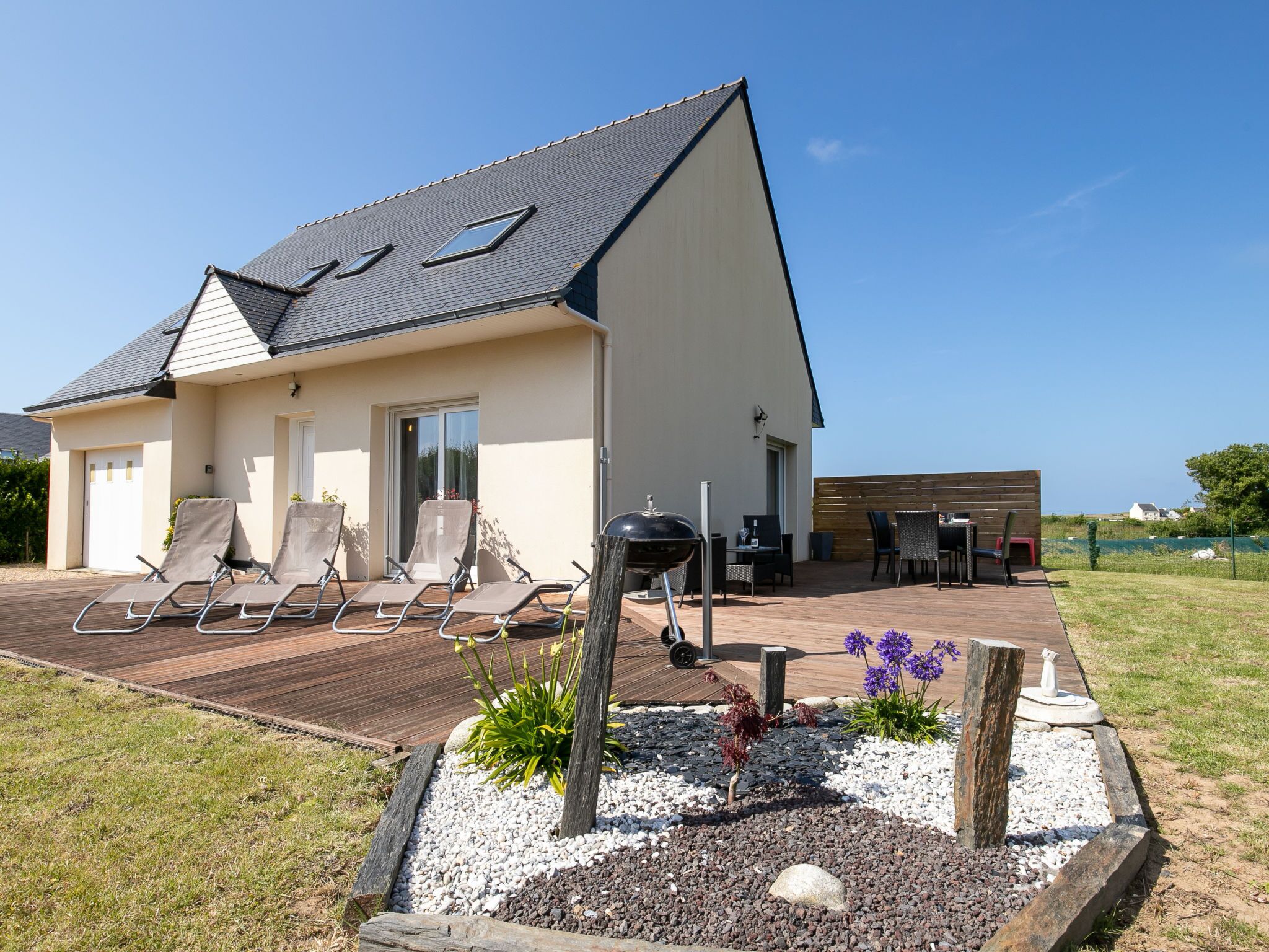 A modern house with a sloped roof, a patio with sun loungers, and a barbecue area.