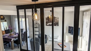 A modern living room with a glass partition, a dining area with purple tablecloth, and a kitchen area with white cabinets. - Chez Patricia et Patrice by Interhome (Guissény)