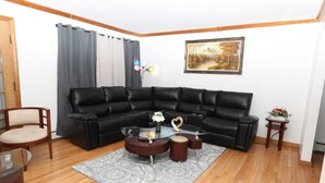 A living room with a black leather sectional sofa, a glass coffee table with a vase and a heart-shaped object, a wooden chair, and a painting on the wall. - Charming 4-bedroom house with WiFi and AC in beautiful Niagara Falls (Niagara Falls)